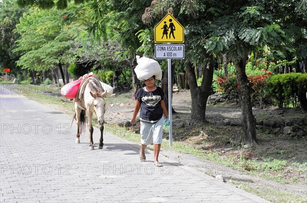 Ometepe Island, Nicaragua, A person carries loads next to a donkey on a sunny road near a road sign