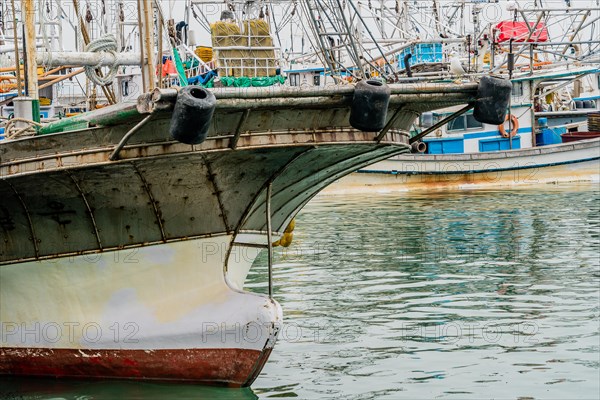 Closeup of bow of large fishing vessel anchored in harbor with other boats and rigging in the