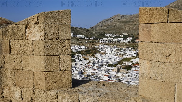 View through an old stone wall to a settlement with white houses and mountains in the background,