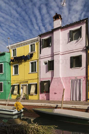 Moored boats on canal lined with pink, yellow and green stucco houses decorated with striped