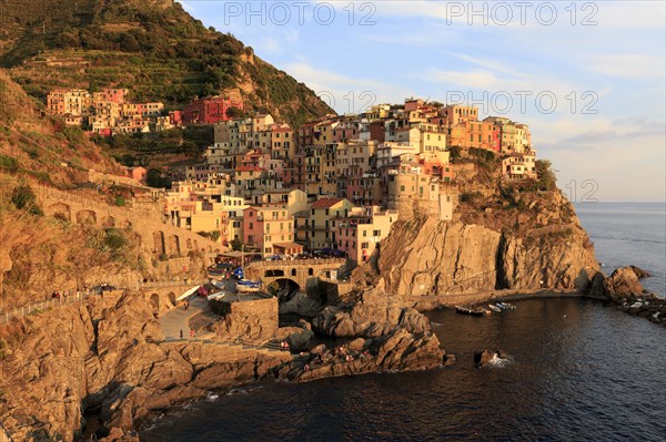 Evening light illuminates Manarola, a picturesque Italian coastal town on cliffs above the sea,