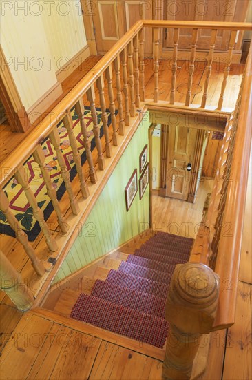 Looking down staircase with maple wood railings and pine wood steps covered with multi-coloured