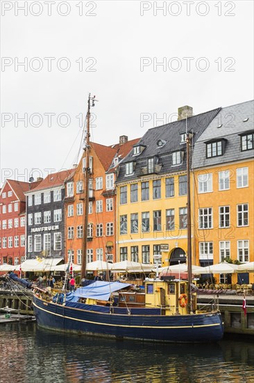 Colourful 17th century apartment buildings and houses with moored blue and yellow sailboat along