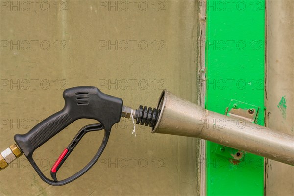 Black handle of car wash high pressure water gun with long nozzle inserted into metal cylinder in