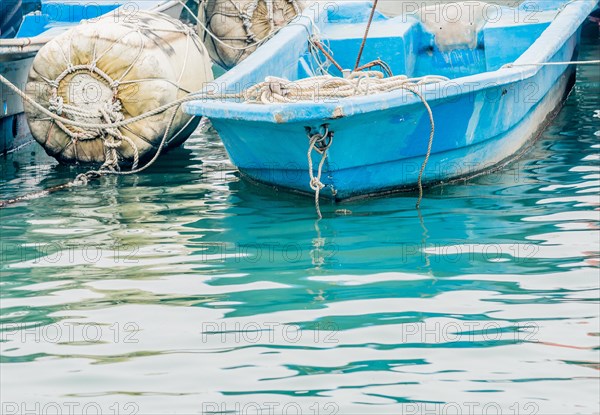 Closeup of small blue fishing boat floating in water tied to a large white buoy in South Korea