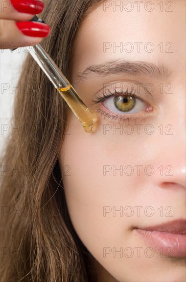 Happy young woman applying serum on her face with her eyes open. Beautiful young Brazilian woman