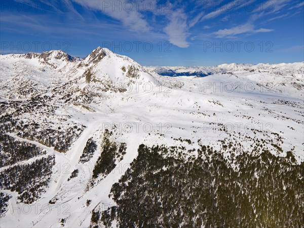 Wide-angle aerial view of snow-covered mountains and forest areas under a blue sky, Grau Roig,