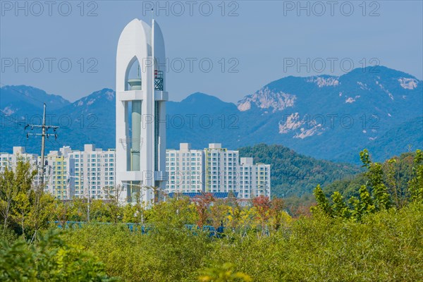 Tall white tower with three sides and cylindrical metal column in middle standing in woodland area