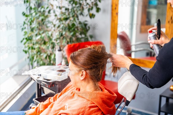 Unrecognizable female hairdresser applying hairspray to a client's hair in the salon