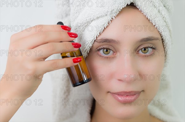 Happy young woman with towel on head holding amber glass bottle of skin serum. Beautiful young