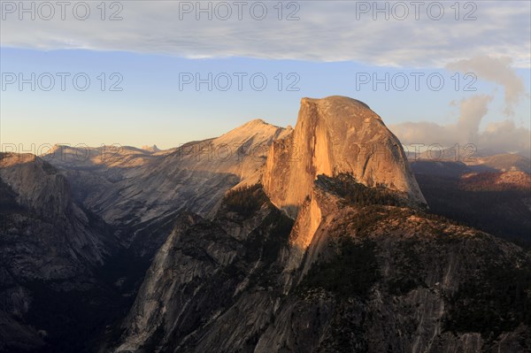 The setting sun bathes Half Dome in orange hues, surrounded by dramatic clouds, Yosemite National