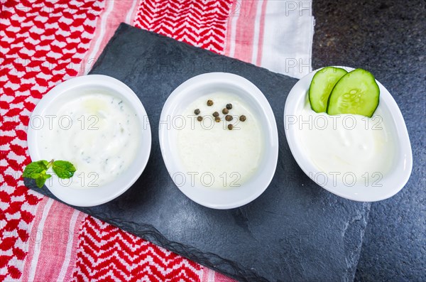 Delicious Lebanese (Arabic) food, thum, labneh and tzatziki sauces on black slate stone background