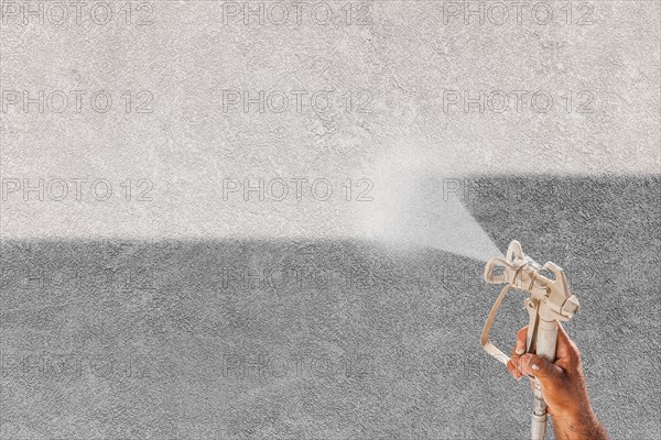 Professional spray painter holding spray gun spraying white paint over grey stucco surface