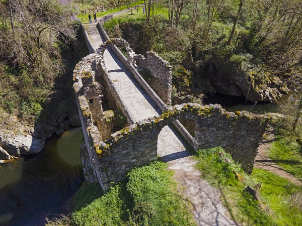 Ruins of a historic bridge with moss-covered stones over a river in a green landscape, Bridge of