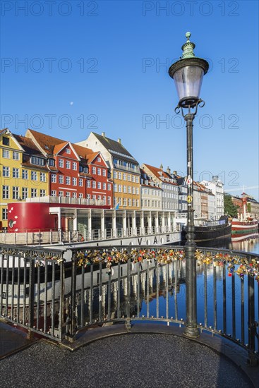 Love locks on black metal railing of canal bridge with antique lamppost, moored boats and colourful