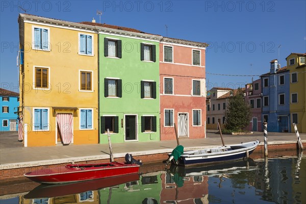 Moored boats on canal lined with orange, green and pink stucco houses decorated with striped