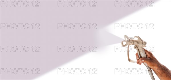 Professional spray painter holding spray gun spraying purple over white surface