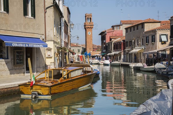Moored boats on canal with colourful residential buildings, houses, shops, tourists and clock tower