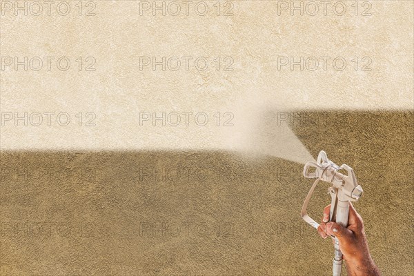Professional spray painter holding spray gun spraying white paint over brown stucco surface