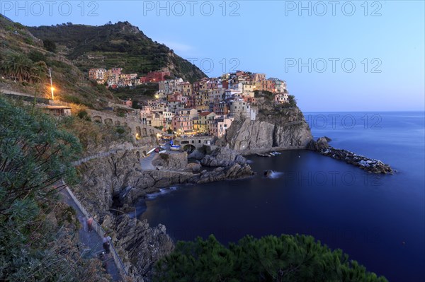 Mediterranean village on rocks on the coast at dusk with lights switched on and calm sea, Italy,