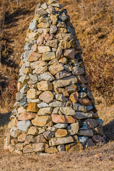 Closeup of pile of stones in the shape of an upside down cone in a public road side park near