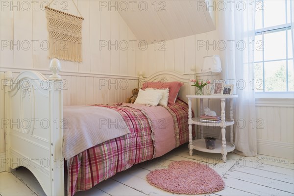 Single bed with red, pink and grey tartan bedspread, white painted antique style wooden headboard