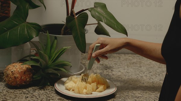 A hand poking a piece of chopped pineapple pieces on a plate with a fork for a healthy vegan summer