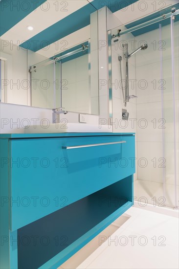 Blue laminated vanity with white rectangular shaped sink, clear glass shower stall in guest