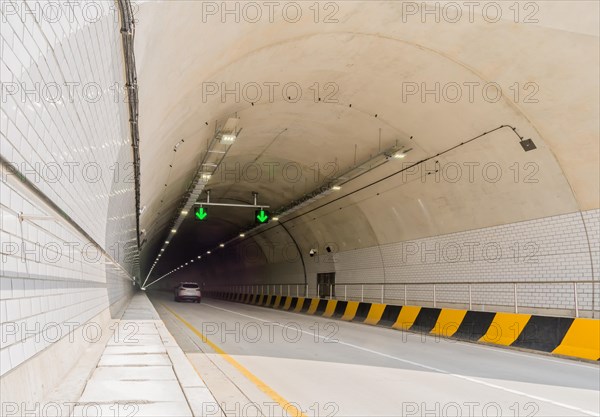 Two lane highway tunnel of white concrete with florescent lights and green arrows on ceiling and