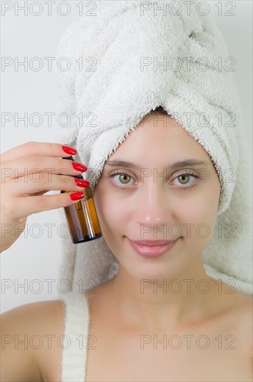 Happy young woman with towel on head holding amber glass bottle of skin serum. Beautiful young