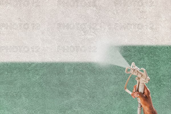Professional spray painter holding spray gun spraying white paint over teal stucco surface