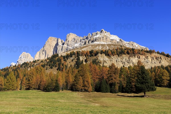 Massive rock formations above a grassland with autumnal trees, Italy, Alto Adige, Bolzano province,