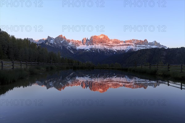 The sunset bathes the mountain peaks in warm light that is reflected in the lake, Trentino-Alto