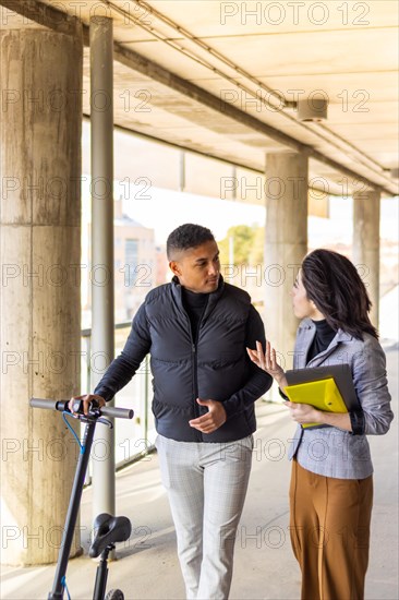 Woman in formal suit talking to man holding a scooter. Girl in formal suit talking to man holding