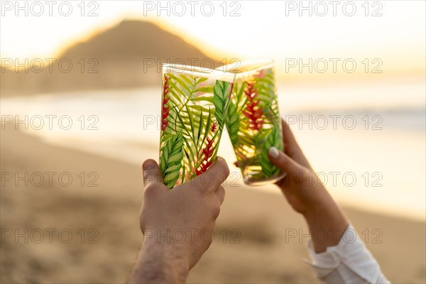 Close-up of hands of lovers toasting with glasses during sunset on the beach