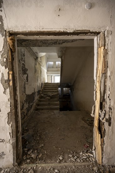 A damaged staircase in a dilapidated building with falling paint and debris at the entrance, ghost