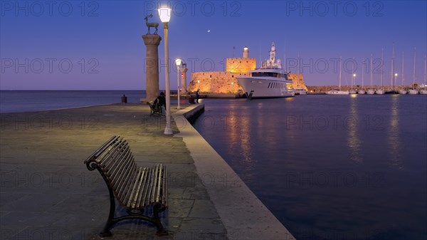 Quiet harbour promenade with bench and lamppost opposite fort and boats in moonlight, night shot,