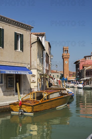 Moored boats on canal with colourful residential buildings, houses, shops, tourists and clock tower