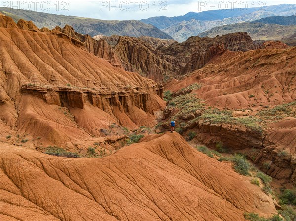 Hiker standing in badlands, gorge with eroded red sandstone rocks, Konorchek Canyon, Boom Gorge,