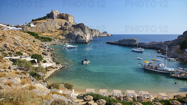 Sunny beach day with a view of a bay, cliffs and parked boats, Paulus Bay, below the Acropolis of
