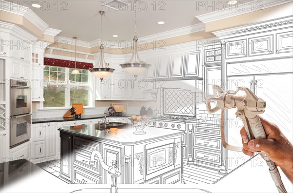 Professional spray painter holding spray gun spraying renovated kitchen over design drawing