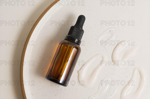 Blank amber glass essential oil (serum) bottle with pipette on cream background. Skin care concept