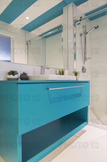 Blue laminated vanity with white rectangular shaped sink, clear glass shower stall in guest