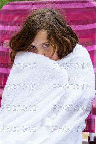 Pretty eight-year-old girl sitting on a chair wrapped in a white towel after getting out of the