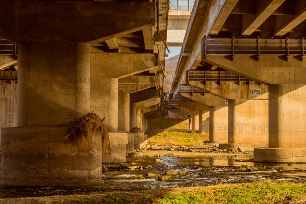 Underside view of columns of two highway overpass next to each other over river in South Korea