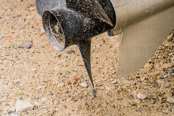 Closeup of black propeller and rudder shaft of outboard engine used to power small boat in South