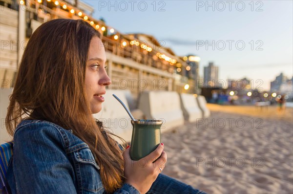 Young girl drinking mate tea tea (chimarrao) on the beach