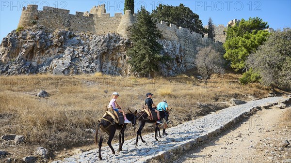 Donkey trail to the Acropolis, children riding donkeys on a dusty hiking trail in front of an old