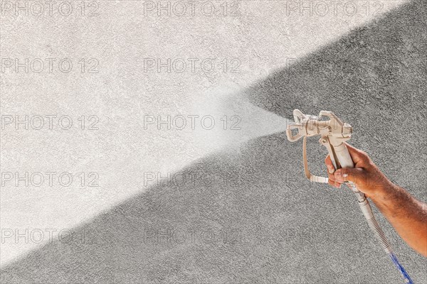 Professional spray painter holding spray gun spraying white paint over grey stucco surface