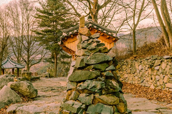 Stone and rock cone shaped tower in front of small wooden oriental building at rural roadside park